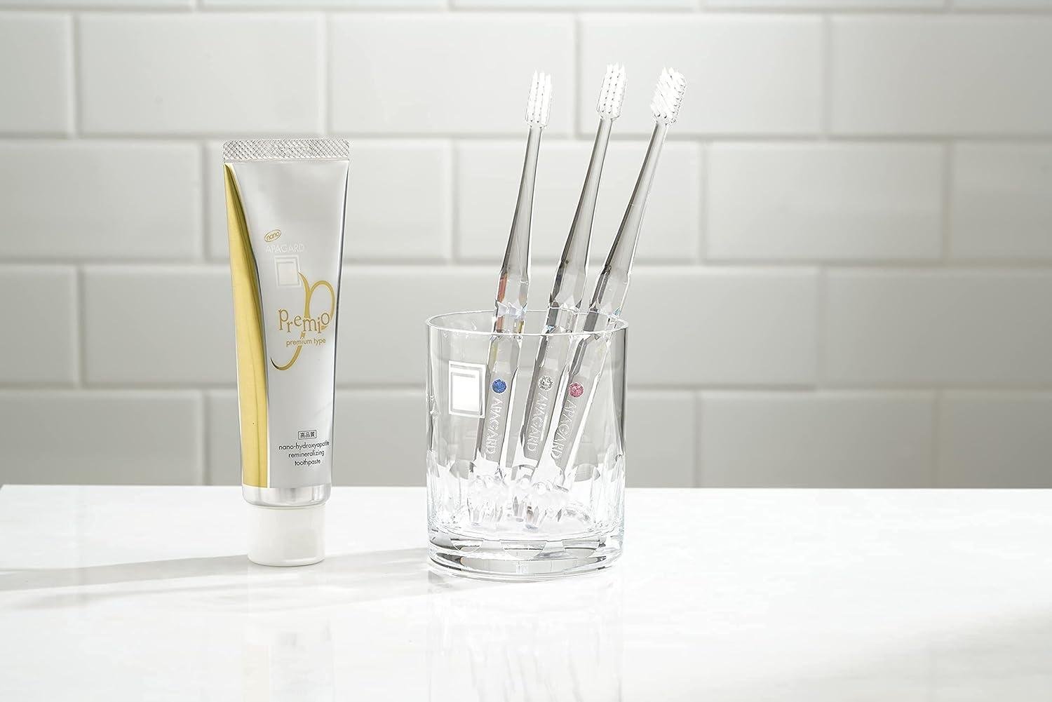 Apagard Premio toothpaste with three toothbrushes on bathroom shelf