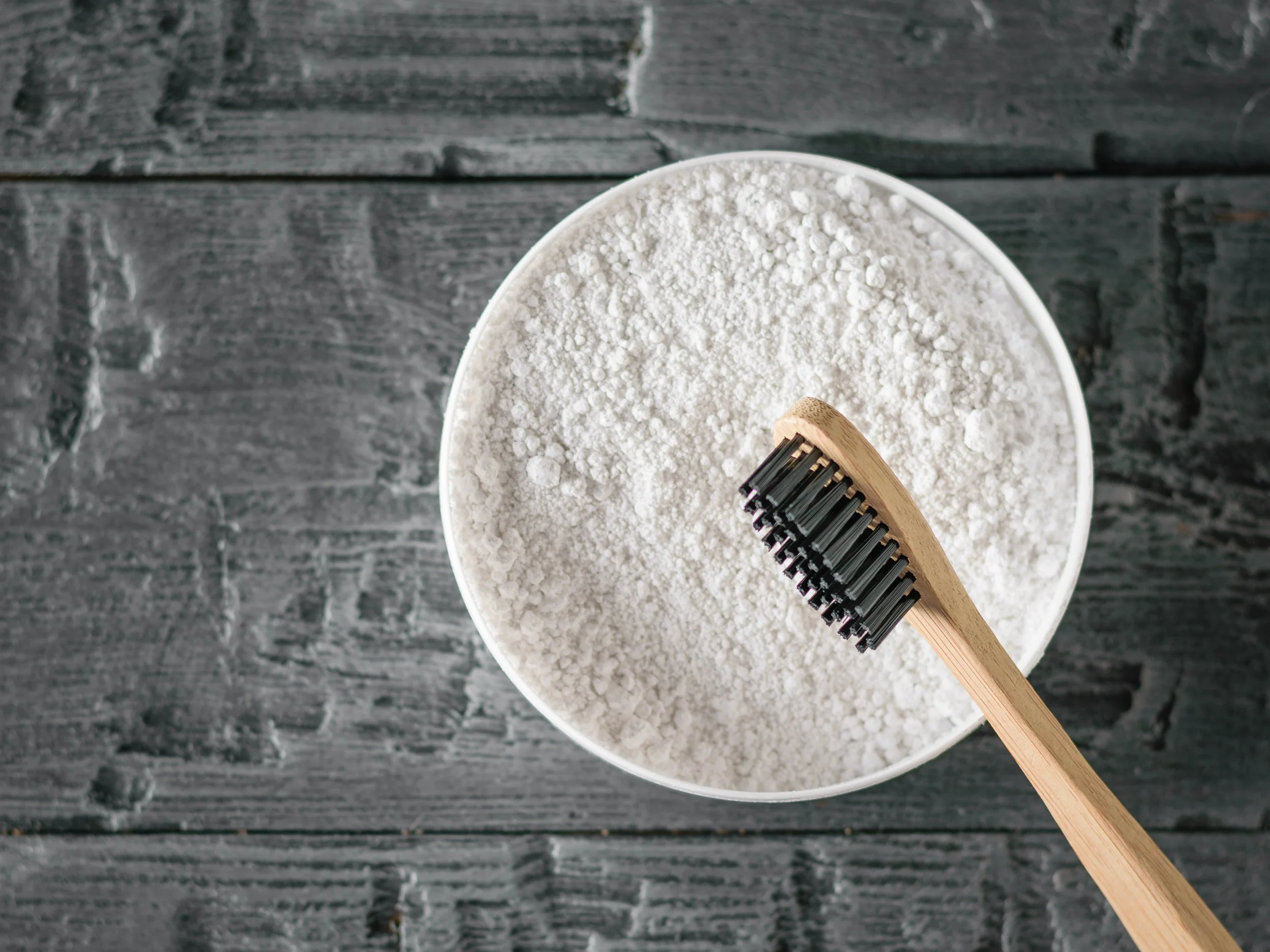 tooth powder in a cup holding colgate powder with bamboo charcoal toothbrush.