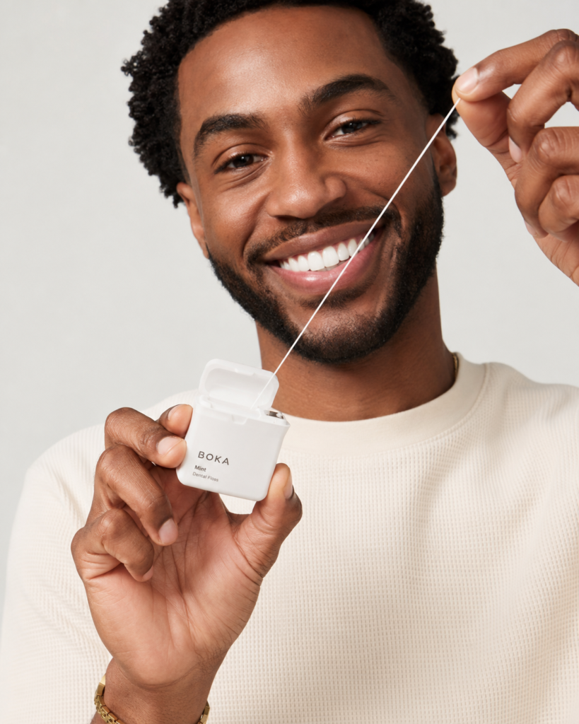 Happy African American man with bright teeth pulling floss from a Boka floss container