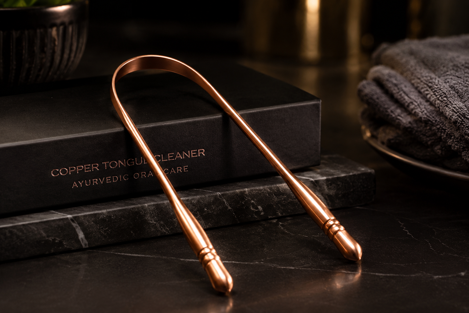 Premium copper tongue scraper displayed on a dark luxury bathroom surface with warm lighting, spa-style towels, and elegant oral care packaging.
