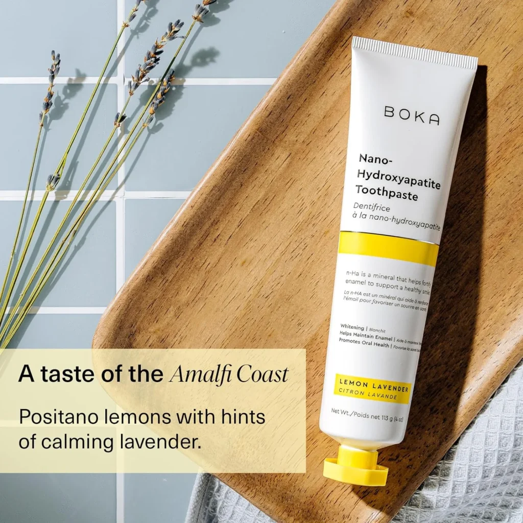 A tube of Boka oral care nano-hydroxyapatite toothpaste resting on a wooden tray next to dried lavender stems, featuring promotional text describing the flavor as a taste of the Amalfi Coast with Positano lemons and calming lavender.