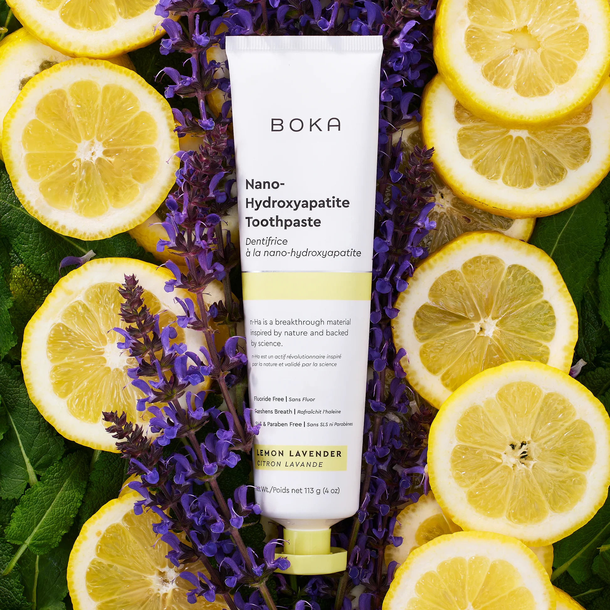 Boka toothpaste lemon lavender hero image displaying a tube of nano-hydroxyapatite toothpaste resting flat on a vibrant background of fresh lemon slices, purple lavender flowers, and green mint leaves.