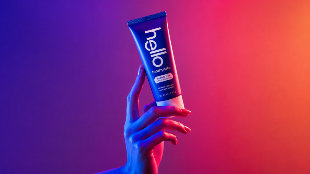 Hello toothpaste tube held by a hand under vibrant blue, pink, and purple neon lighting.